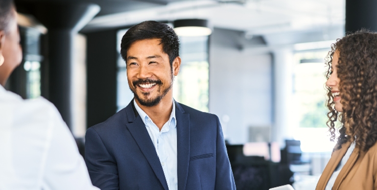 A man in a work suit smiling to a woman in white while another listens in